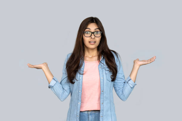 unsure confused young adult indian woman standing isolated on grey background copy space. uncertain doubtful hindu girl client customer doubting choosing looking at camera shrugging shoulders - choice thinking women decisions imagens e fotografias de stock