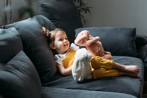 Cute four years old Caucasian girl enjoying lying on couch and hugging her toys.