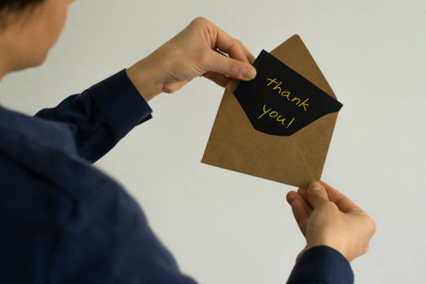Partial view of woman holding kraft envelope with thank you card isolated on white stock photo