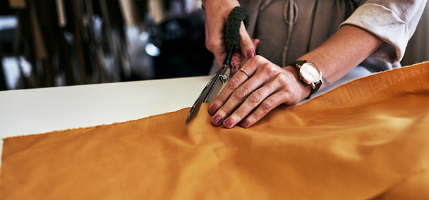 Cropped shot of an unrecognizable fashion designer cutting fabric