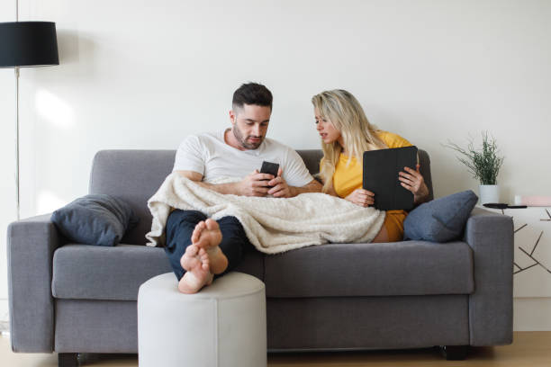 istock Young casual couple using mobiles phone and tablet at home 1205714367