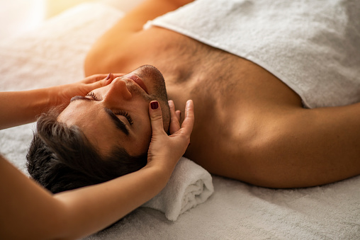 Male beauty - man receiving facial massage at luxury spa. Handsome guy, face massage. Hands of a masseuse working. Handsome man at the spa getting a facial. Man getting a massage at the healthspa
