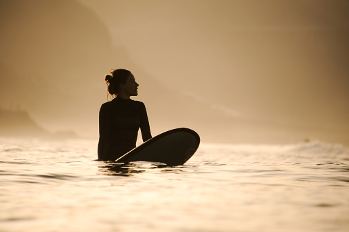 Silhouette of a fit surfer girl with hair bun in the waters