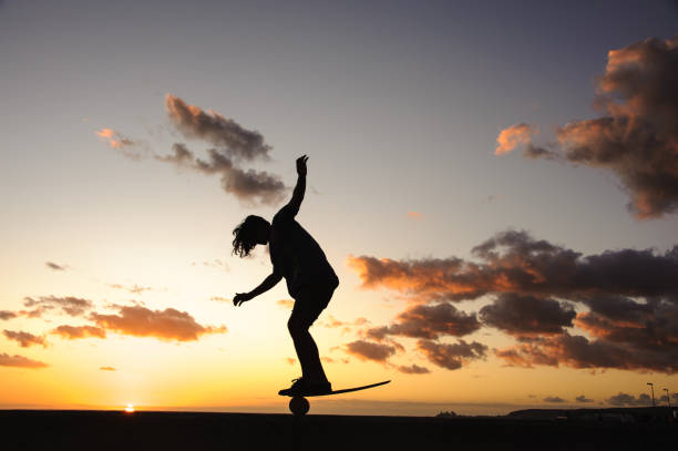 Skateboarder in action. Black silhouette of young boy making air trick with grab on skate in skatepark on sky with sun background. Street culture, skateboard riding lessons. Weekend activities.