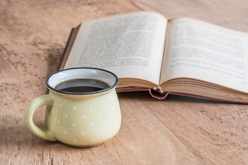 cup of coffee on a wooden table against an opened book