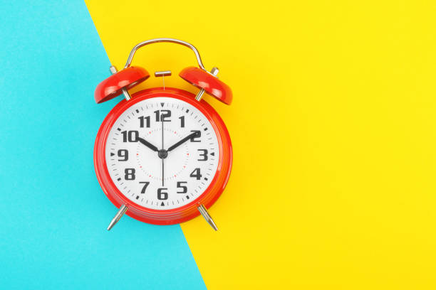 istock Red retro alarm clock with a big dial, on divided diagonally blue-yellow background 1205718451