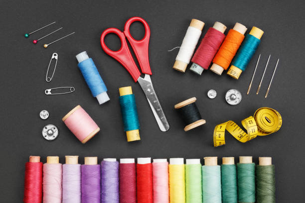 Colored thread coils, scissors, buttons, needles, pin and a tailor meter on a black background. Colored thread coils, scissors, buttons, needles, pin and a tailor meter on a black background. The concept of sewing accessories. Flat layout, top view. sewing thread rolled up creation stock pictures, royalty-free photos & images