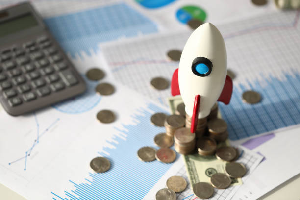 istock Small toy rocket, coins, calculator and official documents at business desk 1205718790
