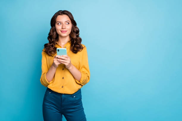 istock Photo of pretty wavy lady holding telephone hands thinking over creative post text idea looking side empty space wear yellow shirt trousers isolated blue color background 1205719040