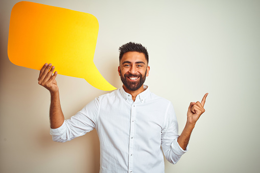 Young arab indian hispanic man holding speech bubble over isolated white background very happy pointing with hand and finger to the side
