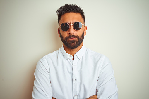 Handsome indian buinessman wearing shirt and sunglasses over isolated white background skeptic and nervous, disapproving expression on face with crossed arms. Negative person.