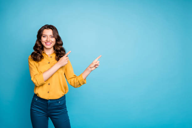 foto de la bella venta gerente señora indicando el dedo vacío espacio aconsejando nuevo producto bajo precio de descuento usar pantalones camisa amarilla sin fondo de color azul aislado - human finger fotografías e imágenes de stock