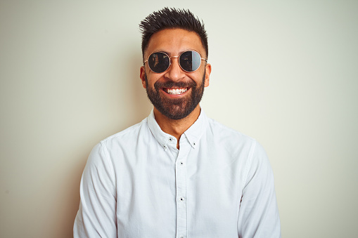 Handsome indian buinessman wearing shirt and sunglasses over isolated white background with a happy and cool smile on face. Lucky person.