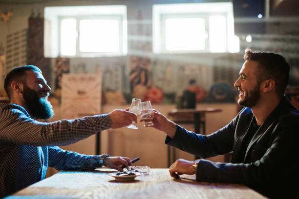 Handsome bearded men drinking whiskey Two Handsome bearded Caucasian elegant men drinking whiskey together in a bar. man cigar stock pictures, royalty-free photos & images