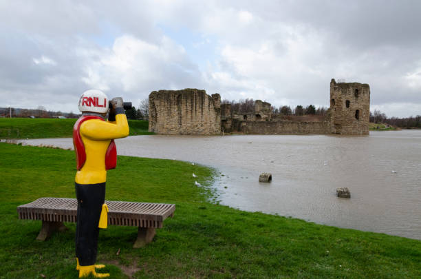 Flint Castle at a high spring tide. Flint, UK: Feb 11, 2020: An unusually high spring tide in the aftermath of storm Ciara sees the River Dee reach the walls of the castle. In the foreground is sculpture by Mike Owen of an RNLI officer. michael owen stock pictures, royalty-free photos & images