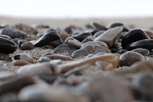 Gray coloured pebbles or gravel horizontal photograph with variety of small and large stones making a rough rustic backdrop with one one big rock in a bed of small stones all over, copy space. Rustic wallpaper template has textured effect and no people.