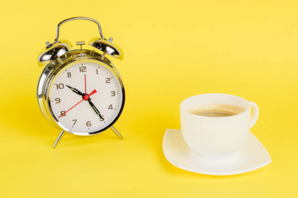 istock Silver alarm clock and cup of coffee on yellow background 1205722588