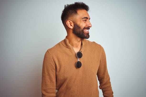 istock Indian man wearing elegant sweater and sunglasses standing over isolated white background looking away to side with smile on face, natural expression. Laughing confident. 1205723194