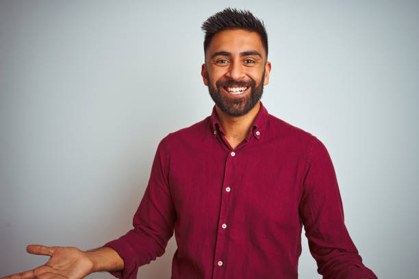 istock Young indian man wearing red elegant shirt standing over isolated grey background smiling cheerful with open arms as friendly welcome, positive and confident greetings 1205723281