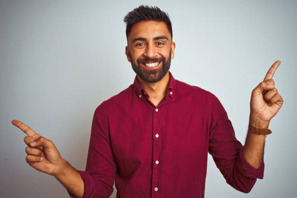 istock Young indian man wearing red elegant shirt standing over isolated grey background smiling confident pointing with fingers to different directions. Copy space for advertisement 1205723361