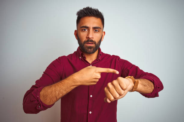 young indian man wearing red elegant shirt standing over isolated grey background in hurry pointing to watch time, impatience, upset and angry for deadline delay - clock face clock deadline human hand imagens e fotografias de stock