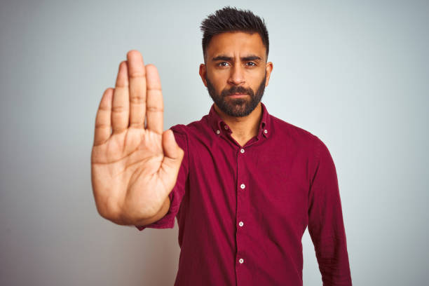 istock Young indian man wearing red elegant shirt standing over isolated grey background doing stop sing with palm of the hand. Warning expression with negative and serious gesture on the face. 1205724314