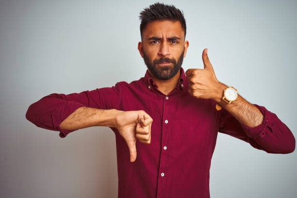 istock Young indian man wearing red elegant shirt standing over isolated grey background Doing thumbs up and down, disagreement and agreement expression. Crazy conflict 1205724502