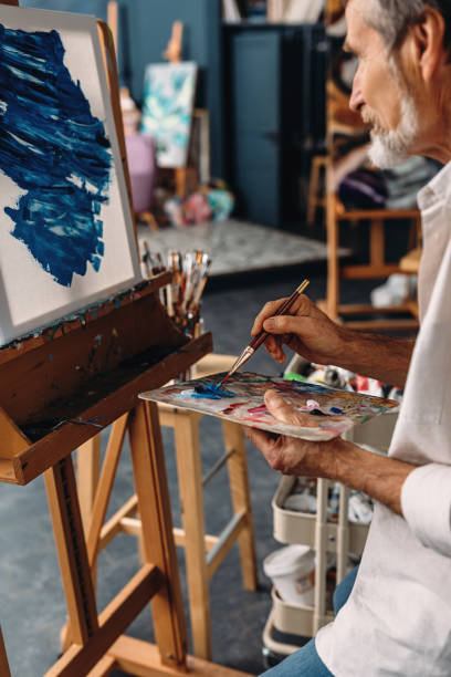 istock Senior artist working in studio. Painter holding a palette and drawing on canvas. 1205726829
