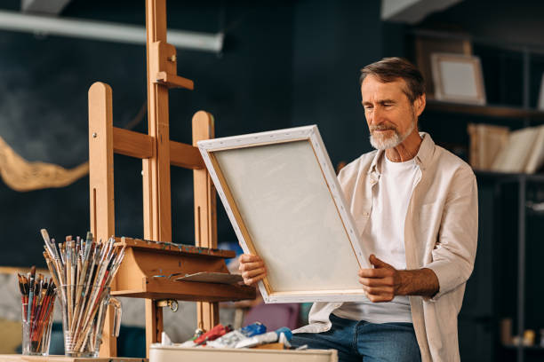 istock Senior painter sitting in his creative studio and holding a canvas with a picture 1205726963