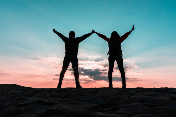 istock Couple silhouette with raised arms holding hands and looking at sunset 1205727441