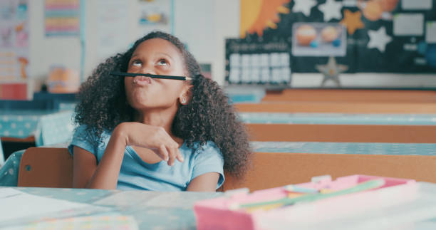 Is it recess yet? Shot of a young girl looking bored while playing at a school desk mischief stock pictures, royalty-free photos & images