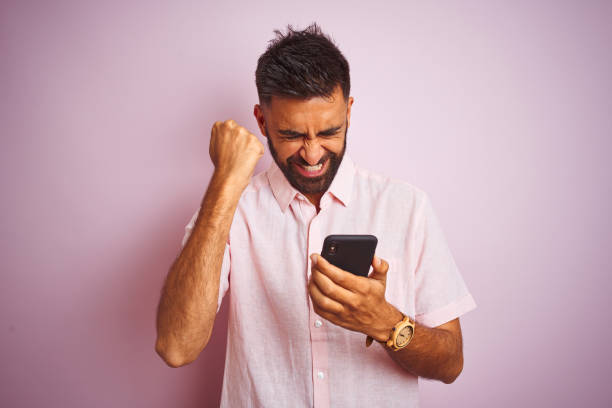istock Young indian man using smartphone standing over isolated pink background annoyed and frustrated shouting with anger, crazy and yelling with raised hand, anger concept 1205733185