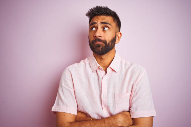 jeune homme indien utilisant la chemise occasionnelle restant au-dessus du fond rose isolé regardant au côté et regardant loin pensant. - one person staring people smart casual photos et images de collection