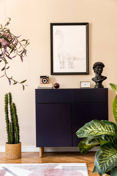 istock Modern composition of home staging with navy blue commode, plants, cacti, mock up poster frame, design carpet and elegant personal accessories. Beige walls. Stylish living room. Home decor. Template. 1205733332