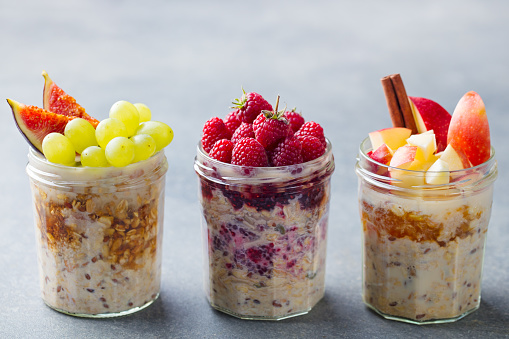 Assortment overnight oats, bircher muesli with fresh berries and fruits in a glass jars. Grey background.