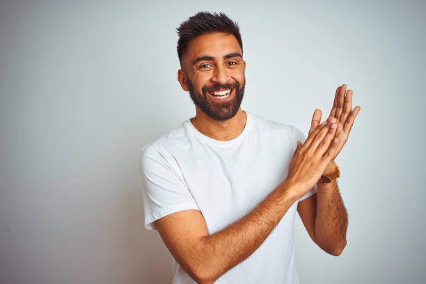 孤立した白い背景の上に立っているtシャツを着た若いインド人男性が拍手し、幸せで喜びに拍手し、一緒に誇り高い手を笑顔で - 南ヨーロッパ民族 ストックフォトと画像