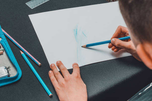 istock A schoolboy draws pencils on white paper. 1205736801