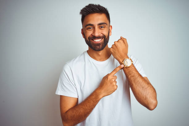 Young indian man wearing t-shirt standing over isolated white background In hurry pointing to watch time, impatience, looking at the camera with relaxed expression Young indian man wearing t-shirt standing over isolated white background In hurry pointing to watch time, impatience, looking at the camera with relaxed expression checking the time stock pictures, royalty-free photos & images