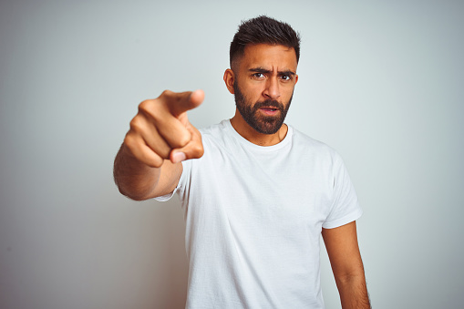 Young indian man wearing t-shirt standing over isolated white background pointing displeased and frustrated to the camera, angry and furious with you