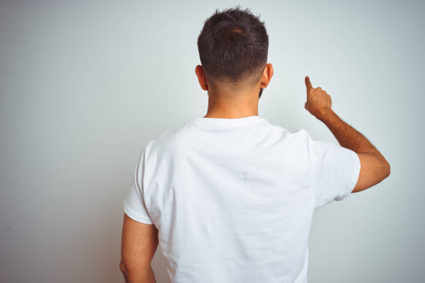 istock Young indian man wearing t-shirt standing over isolated white background Posing backwards pointing ahead with finger hand 1205737941