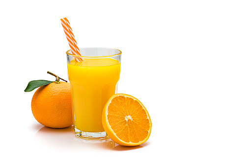 Front view of an orange juice glass shot on reflective white background. Two drinking straws are in the glass. Whole and sliced range fruits are beside the glass. The composition is at the left of an horizontal frame leaving useful copy space for text and/or logo at the right. Predominant colors are orange and white. High resolution 42Mp studio digital capture taken with Sony A7rii and Sony FE 90mm f2.8 macro G OSS lens