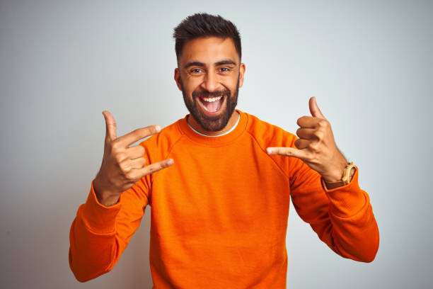 istock Young indian man wearing orange sweater over isolated white background shouting with crazy expression doing rock symbol with hands up. Music star. Heavy concept. 1205739746