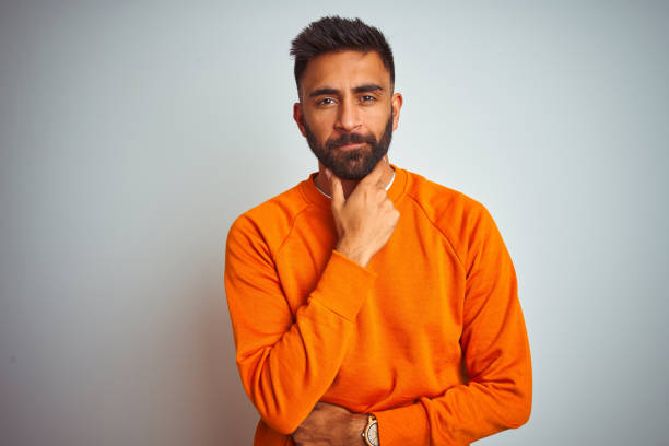 istock Young indian man wearing orange sweater over isolated white background looking confident at the camera with smile with crossed arms and hand raised on chin. Thinking positive. 1205739961