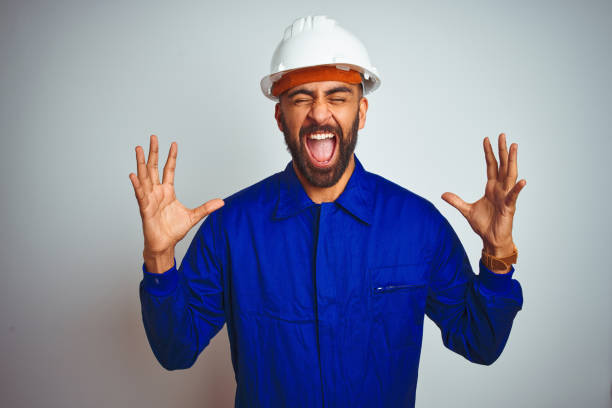 istock Handsome indian worker man wearing uniform and helmet over isolated white background celebrating mad and crazy for success with arms raised and closed eyes screaming excited. Winner concept 1205740716