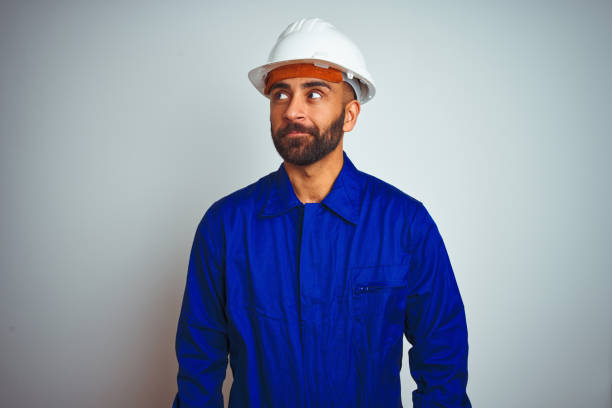 istock Handsome indian worker man wearing uniform and helmet over isolated white background smiling looking to the side and staring away thinking. 1205740729