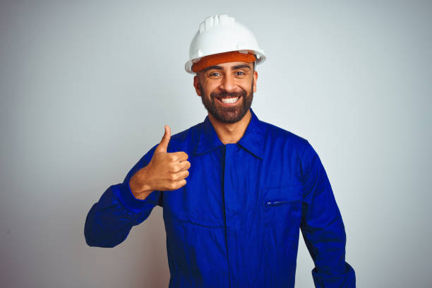 istock Handsome indian worker man wearing uniform and helmet over isolated white background doing happy thumbs up gesture with hand. Approving expression looking at the camera showing success. 1205740776