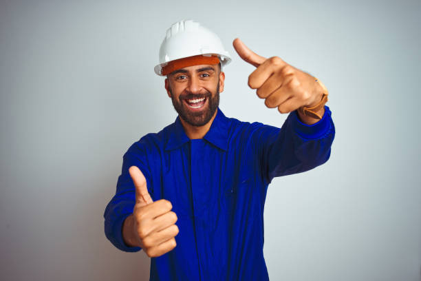 istock Handsome indian worker man wearing uniform and helmet over isolated white background approving doing positive gesture with hand, thumbs up smiling and happy for success. Winner gesture. 1205740809