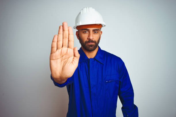 istock Handsome indian worker man wearing uniform and helmet over isolated white background doing stop sing with palm of the hand. Warning expression with negative and serious gesture on the face. 1205740819