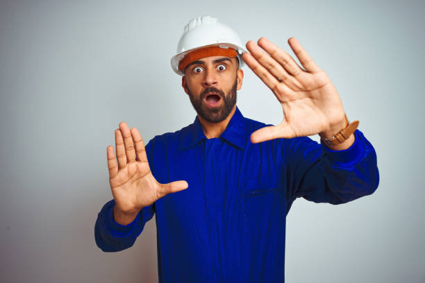 istock Handsome indian worker man wearing uniform and helmet over isolated white background afraid and terrified with fear expression stop gesture with hands, shouting in shock. Panic concept. 1205740853