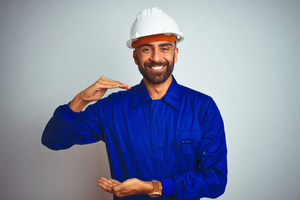 istock Handsome indian worker man wearing uniform and helmet over isolated white background gesturing with hands showing big and large size sign, measure symbol. Smiling looking at the camera. Measuring concept. 1205740854